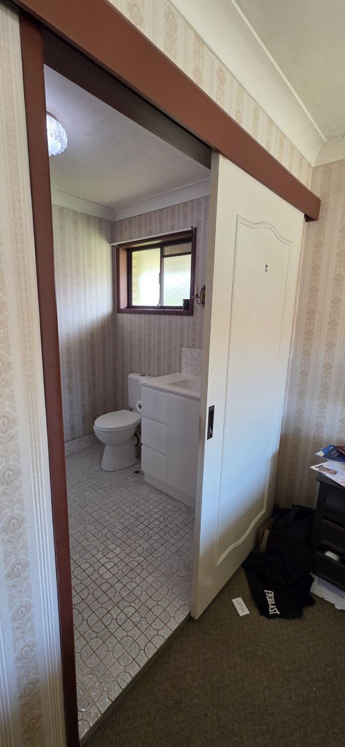 Wishart ensuite before renovation with patterned flooring, toilet and white vanity