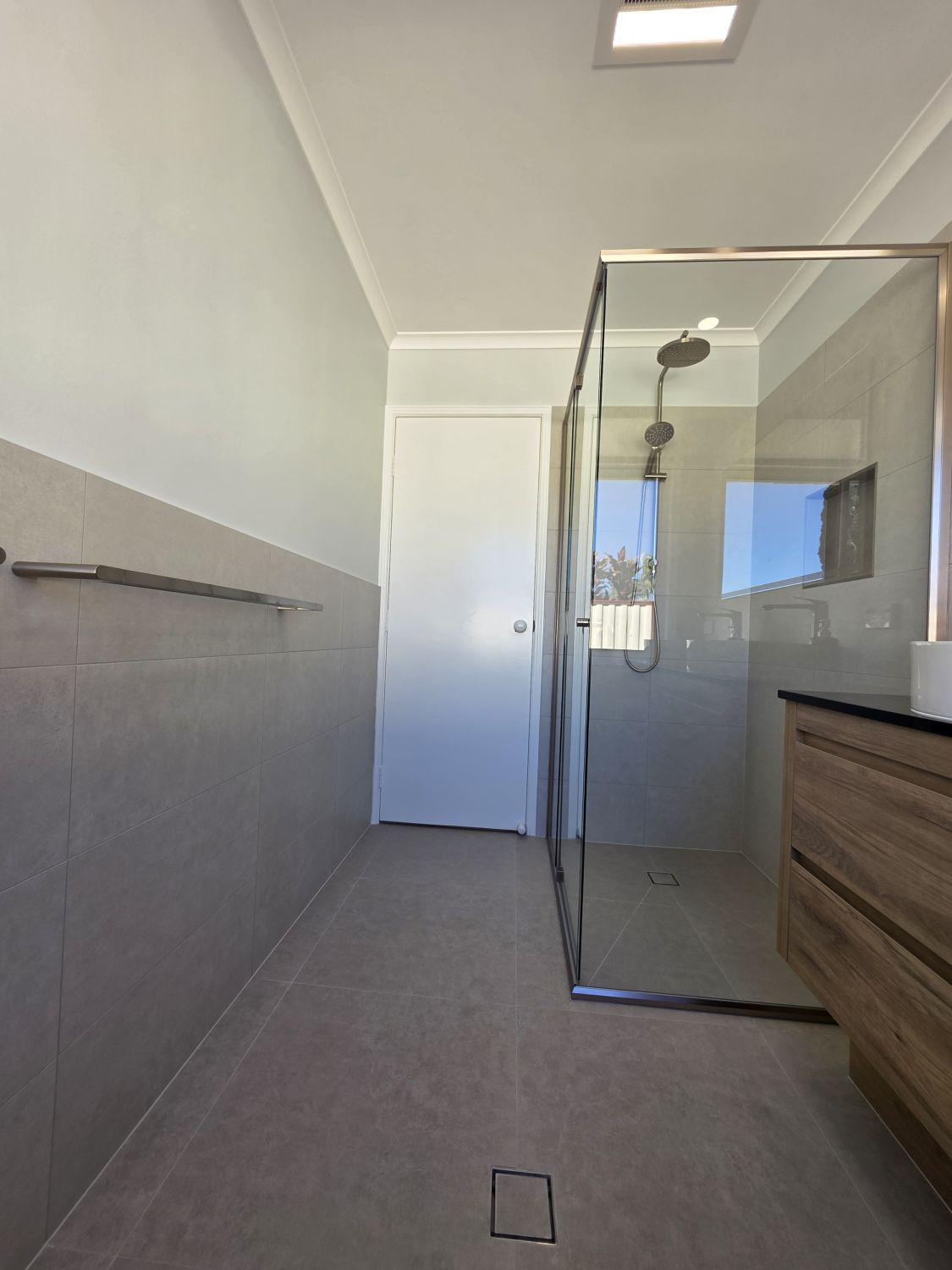 Calamvale bathroom after renovation with continuous grey floor and glass shower