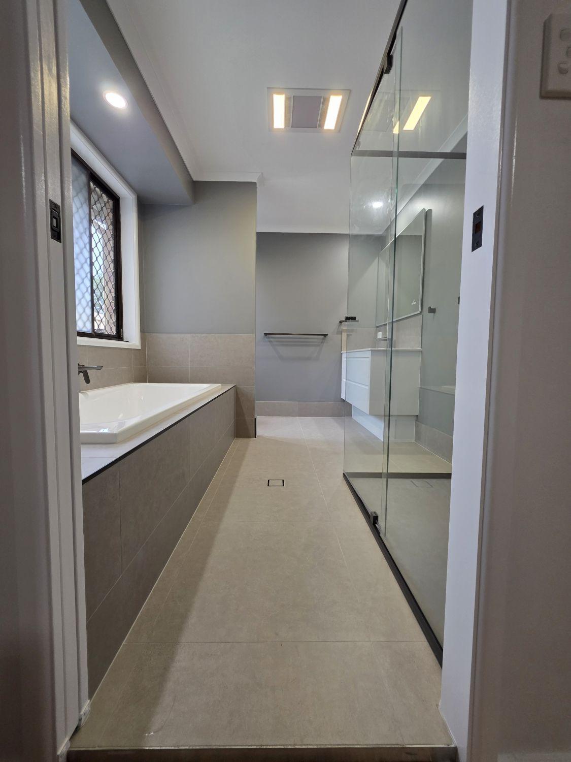 First Karana Downs bathroom after renovation with tiled bath, glass shower and white vanity